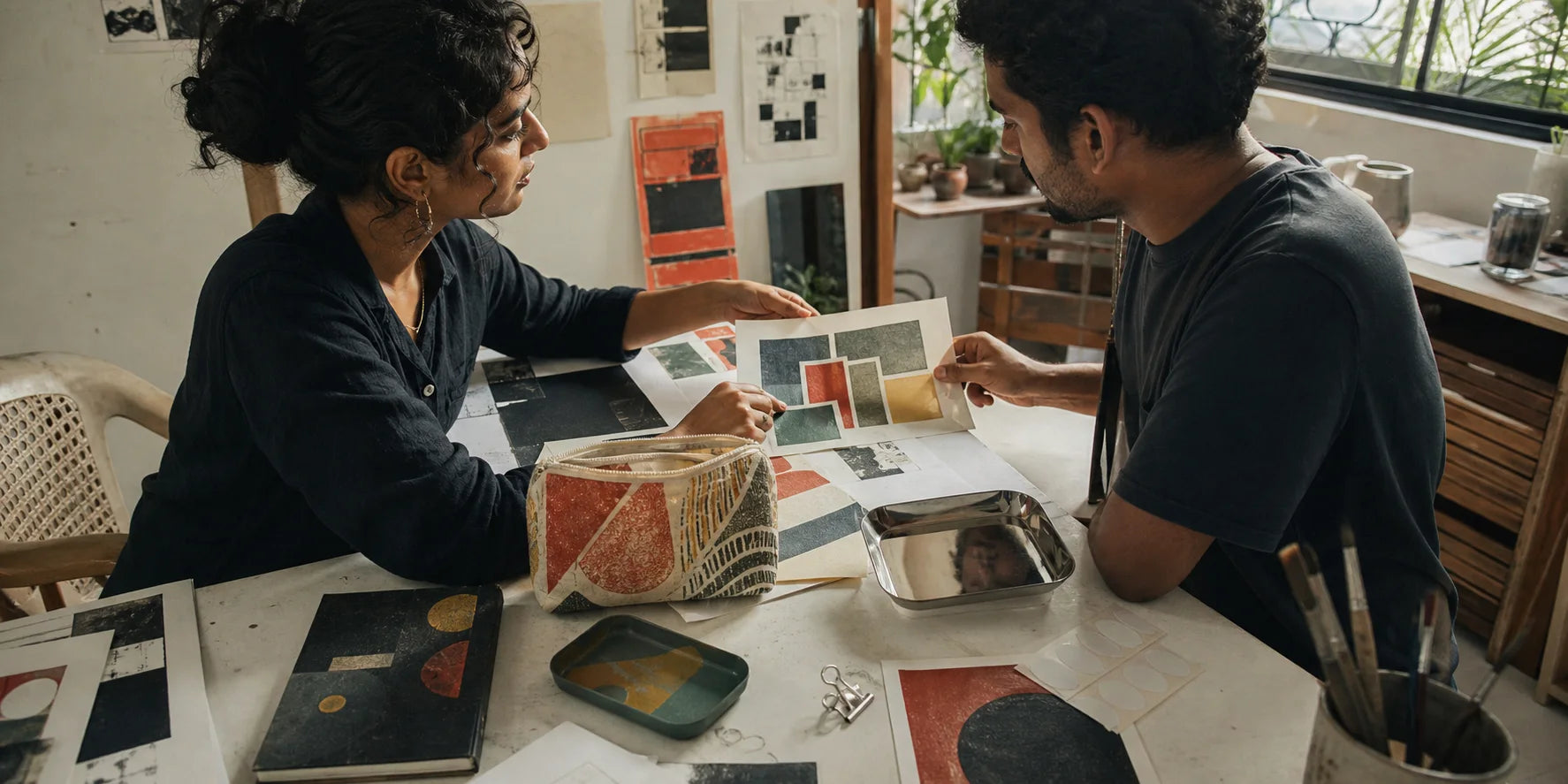 Two Indian printmakers reviewing original geometric work in a sunlit Kochi studio