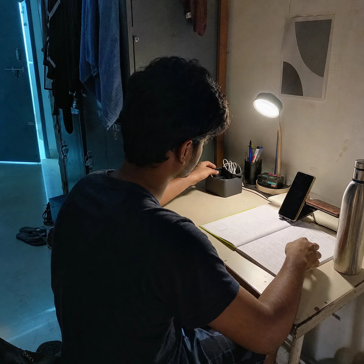 Indian student using a phone stand and cable organiser at a compact hostel desk