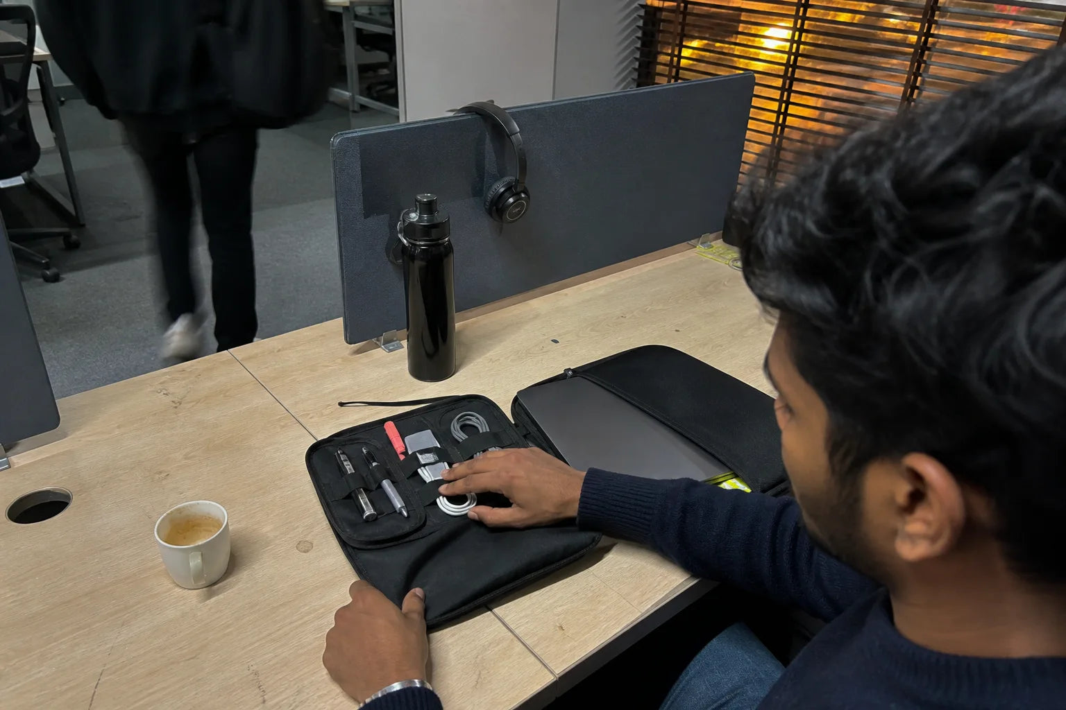 Indian young professional packing a cable organiser and laptop sleeve at a shared desk