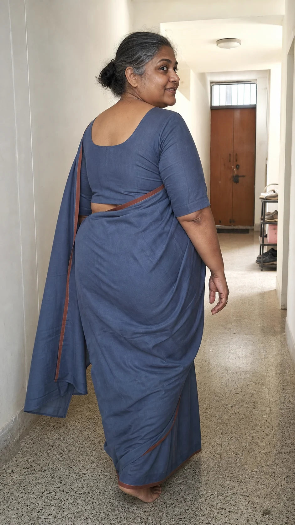 Generated editorial fit study showing the back drape and shoulder fit of a muted indigo saree in an apartment corridor