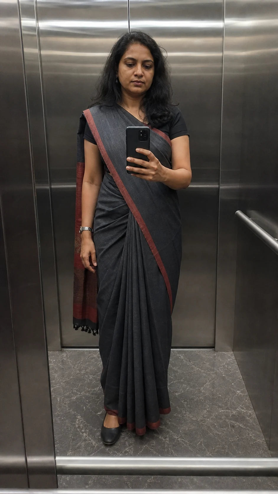 Generated editorial fit study of an Indian professional taking a lift mirror photograph in a charcoal saree