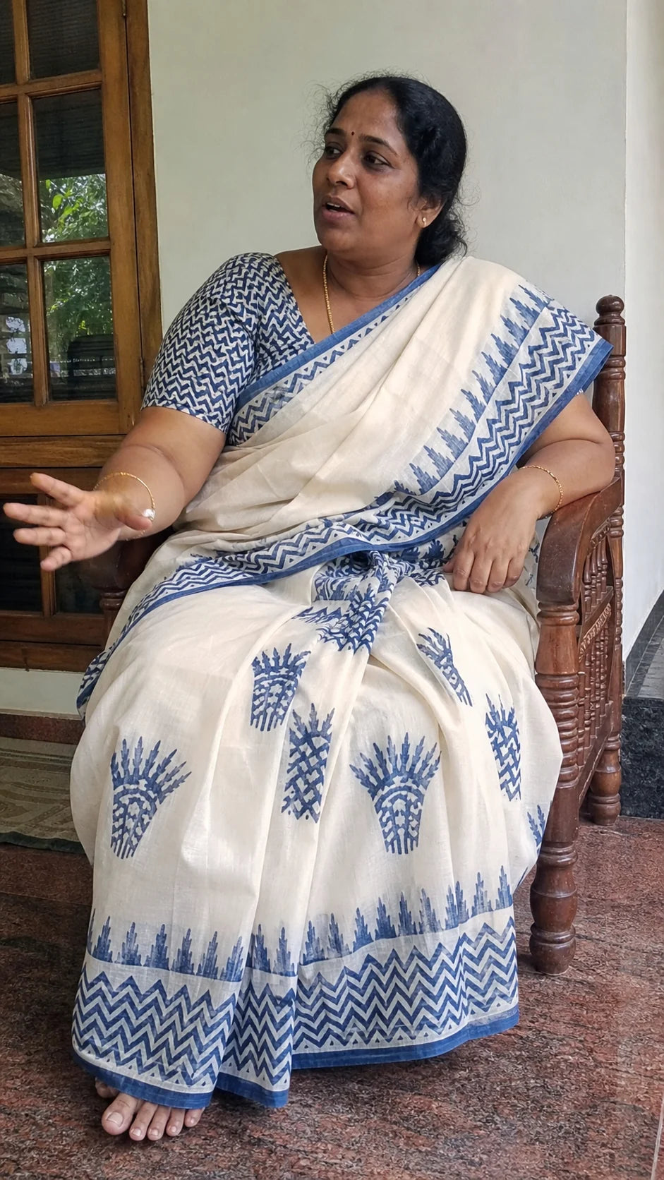 Generated editorial fit study of a fuller-bodied Indian woman seated on a veranda in an ivory and indigo saree